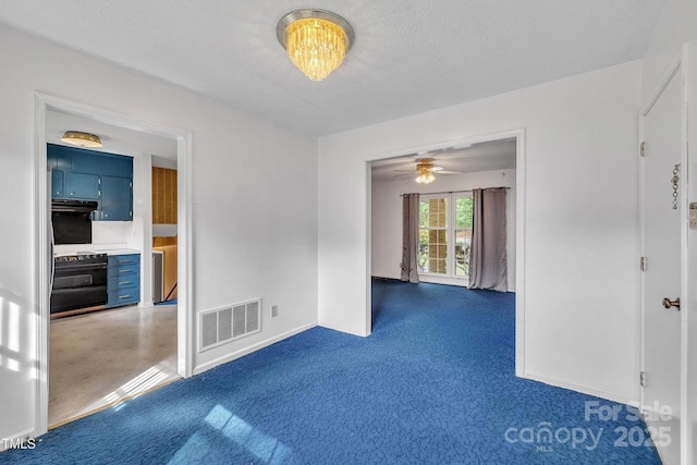 spare room with a textured ceiling, visible vents, ceiling fan, baseboards, and dark carpet