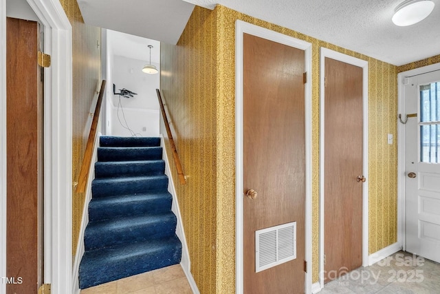 staircase with a textured ceiling, visible vents, tile patterned flooring, baseboards, and wallpapered walls