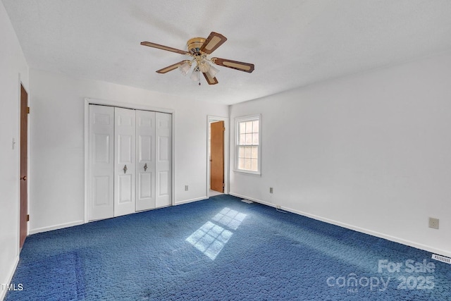 unfurnished bedroom with a closet, visible vents, ceiling fan, baseboards, and dark carpet