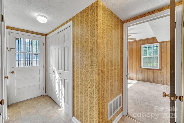 corridor featuring a textured ceiling, visible vents, and wooden walls