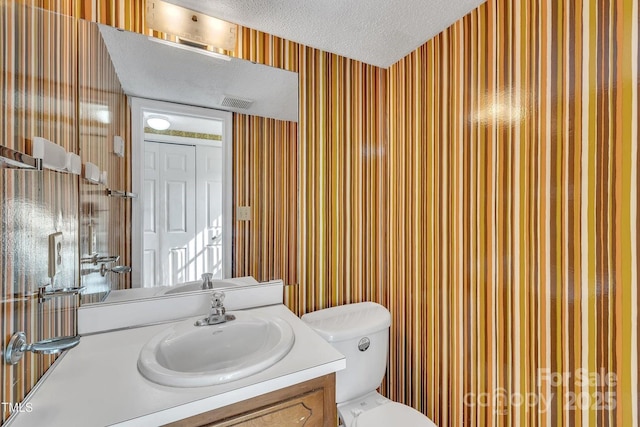 bathroom featuring wallpapered walls, a textured ceiling, toilet, visible vents, and vanity