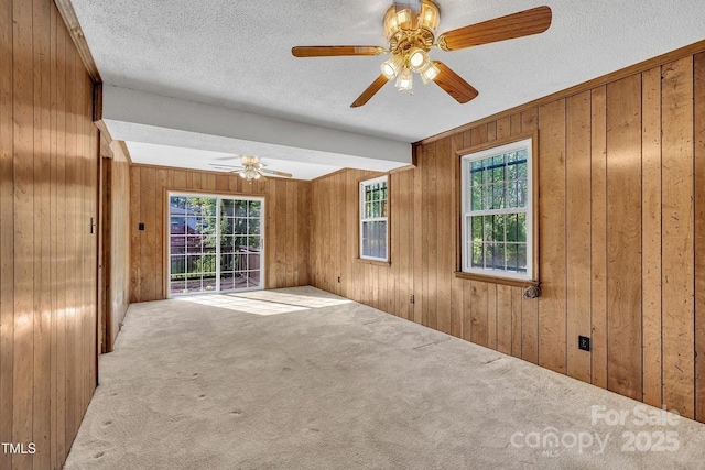 carpeted empty room featuring a ceiling fan, wooden walls, and a healthy amount of sunlight
