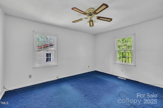 carpeted empty room with a textured ceiling, baseboards, a ceiling fan, and visible vents