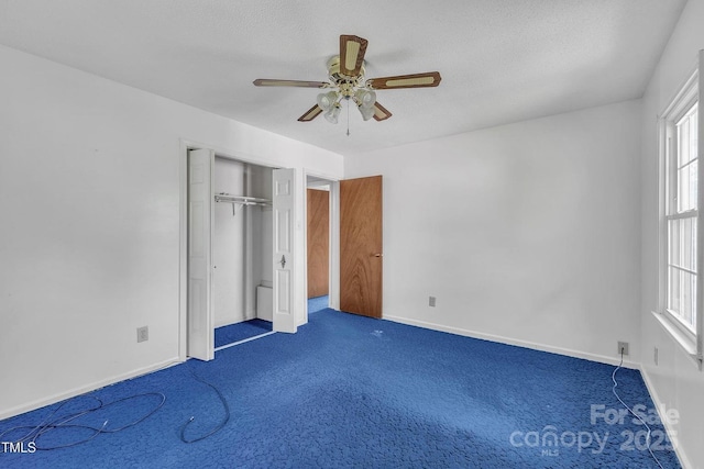 unfurnished bedroom with a textured ceiling, dark colored carpet, baseboards, and ceiling fan