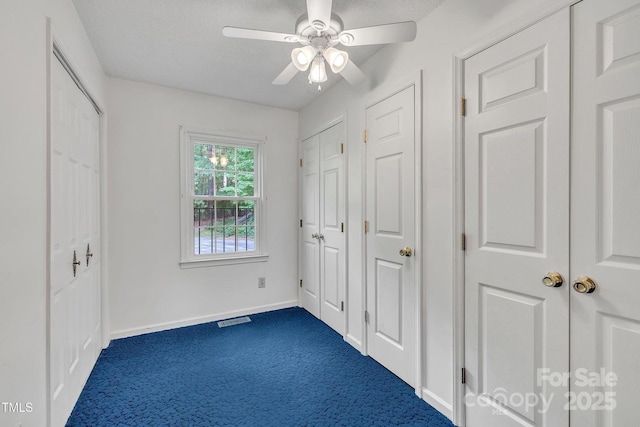 unfurnished bedroom with multiple closets, visible vents, baseboards, ceiling fan, and dark colored carpet