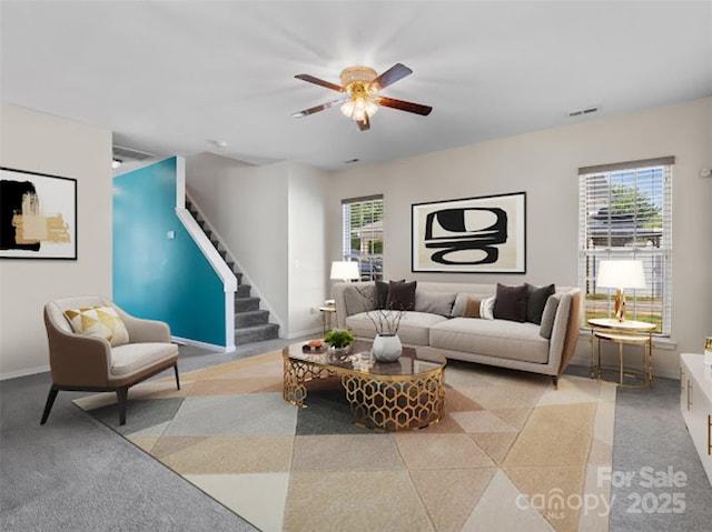living area with healthy amount of natural light, ceiling fan, stairway, and baseboards