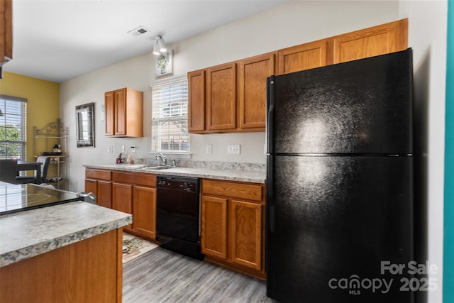 kitchen featuring black appliances, light wood finished floors, light countertops, a sink, and brown cabinets