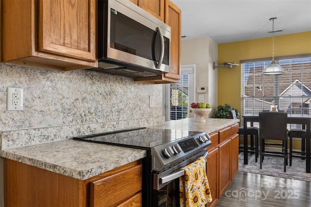 kitchen with appliances with stainless steel finishes, wood finished floors, decorative backsplash, brown cabinets, and light countertops