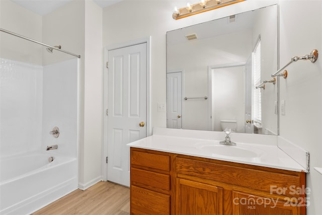 bathroom featuring wood finished floors, toilet, vanity, bathtub / shower combination, and baseboards