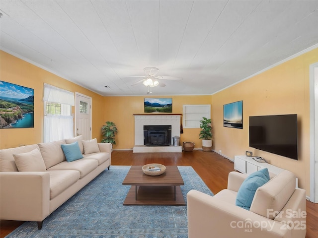 living room featuring wood finished floors, crown molding, ceiling fan, and a glass covered fireplace