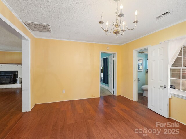 empty room with a chandelier, wood finished floors, a textured ceiling, ornamental molding, and a fireplace