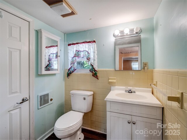 bathroom featuring tile walls, toilet, vanity, and a wainscoted wall