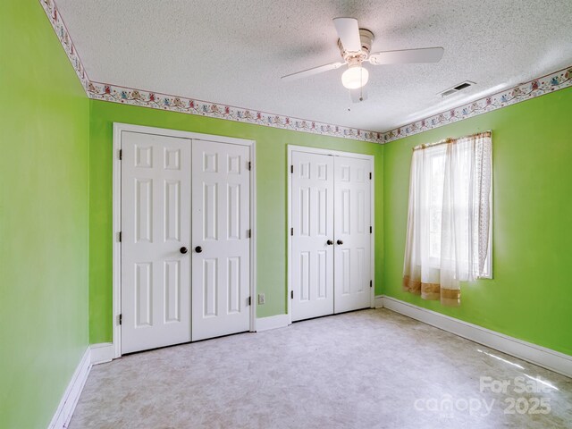 unfurnished bedroom with two closets, a textured ceiling, baseboards, and carpet flooring