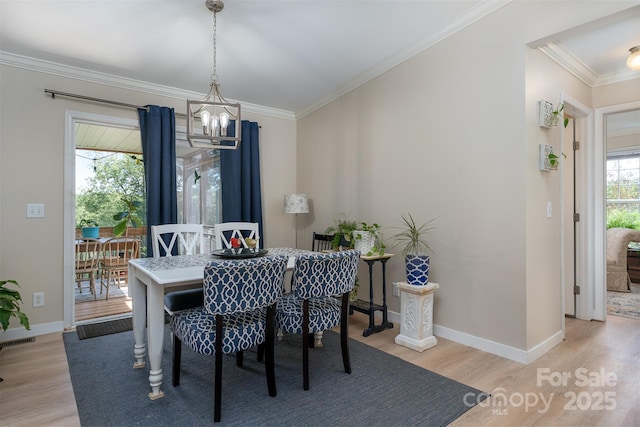 dining area with light wood-style floors, a chandelier, and ornamental molding