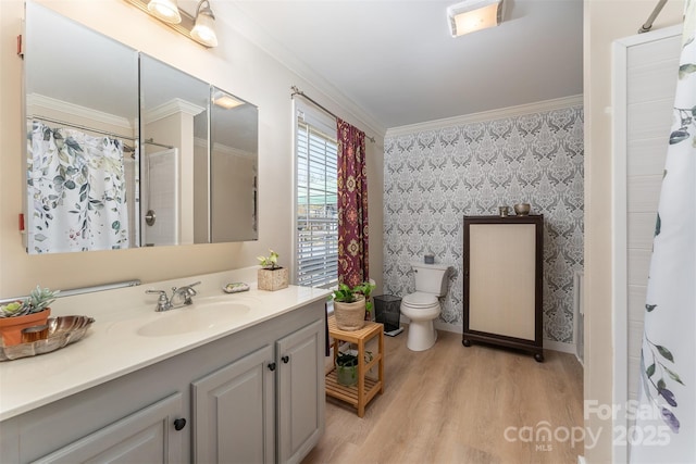 bathroom with toilet, wood finished floors, vanity, ornamental molding, and wallpapered walls