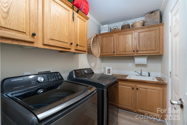 washroom with a sink, washer and clothes dryer, cabinet space, crown molding, and light wood finished floors
