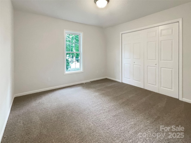 unfurnished bedroom with a closet, baseboards, and dark carpet