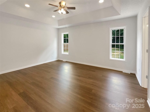spare room with a ceiling fan, dark wood-type flooring, a raised ceiling, and recessed lighting
