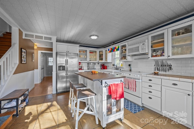 25 Alpine Way, Clyde, NC 28721 - kitchen featuring white appliances, a breakfast bar area, white cabinets, glass insert cabinets, and a wainscoted wall
