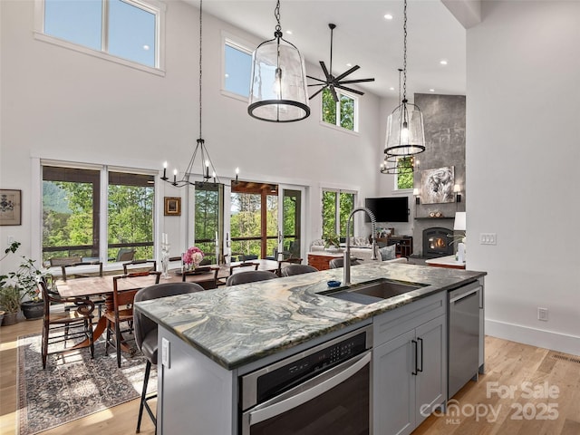 kitchen featuring stainless steel dishwasher, light wood finished floors, a kitchen island with sink, and a sink