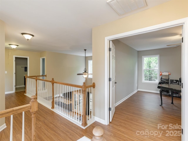 corridor featuring wood finished floors, baseboards, an upstairs landing, and visible vents