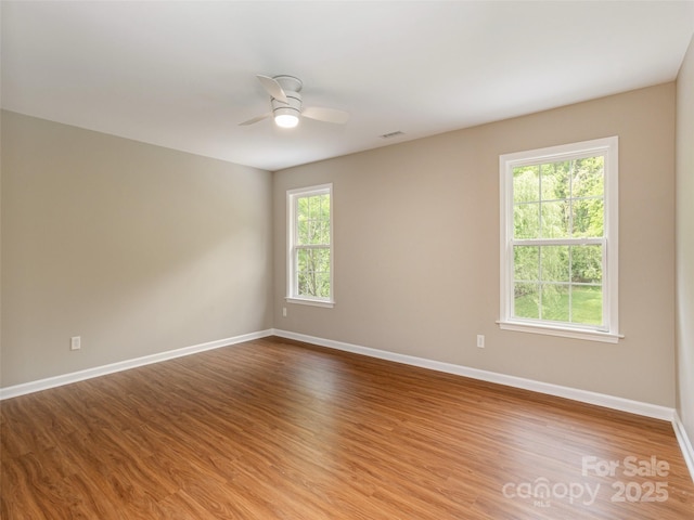 spare room with wood finished floors, visible vents, baseboards, and a ceiling fan