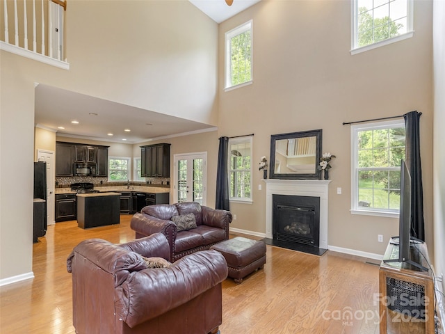 living area with baseboards, light wood-style flooring, a towering ceiling, and a glass covered fireplace