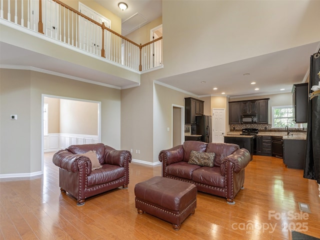 living area with crown molding, a high ceiling, baseboards, and light wood-type flooring