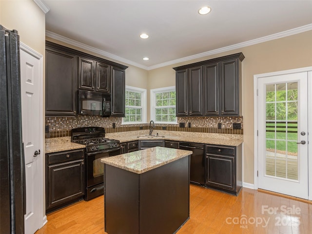 kitchen featuring a sink, light stone counters, black appliances, backsplash, and light wood-style floors