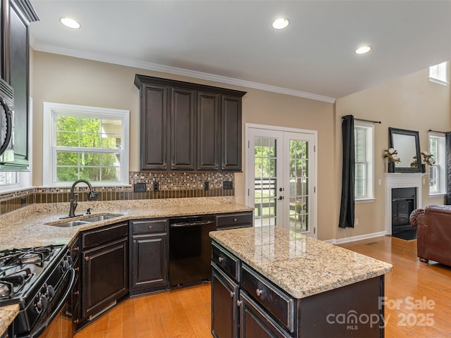 kitchen featuring a sink, light stone counters, black appliances, open floor plan, and light wood-style floors