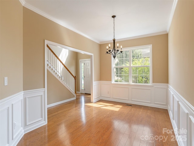 spare room with a decorative wall, stairway, an inviting chandelier, light wood-style flooring, and wainscoting