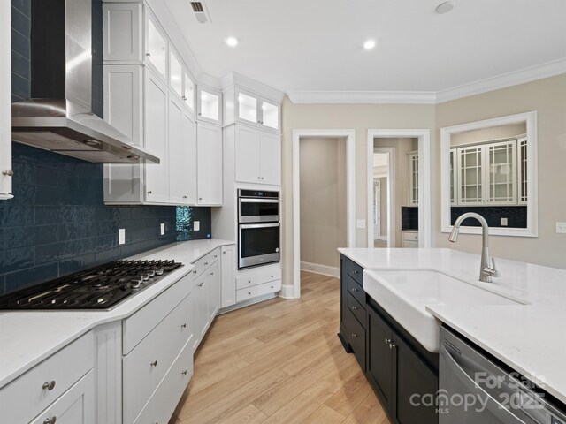 709 Cavesson Way, Monroe, NC 28110 - kitchen featuring stainless steel appliances, wall chimney exhaust hood, crown molding, white cabinets, and light wood-type flooring
