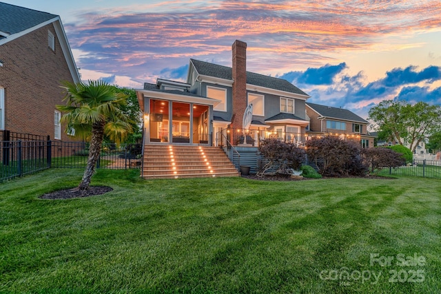 back of property at dusk with a sunroom, a chimney, a lawn, a fenced backyard, and stairs