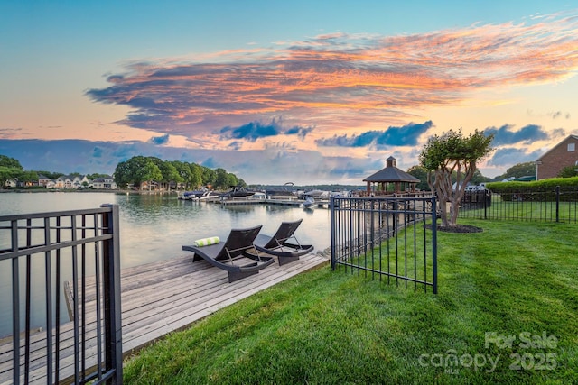 view of dock with a gazebo, fence, a water view, and a lawn