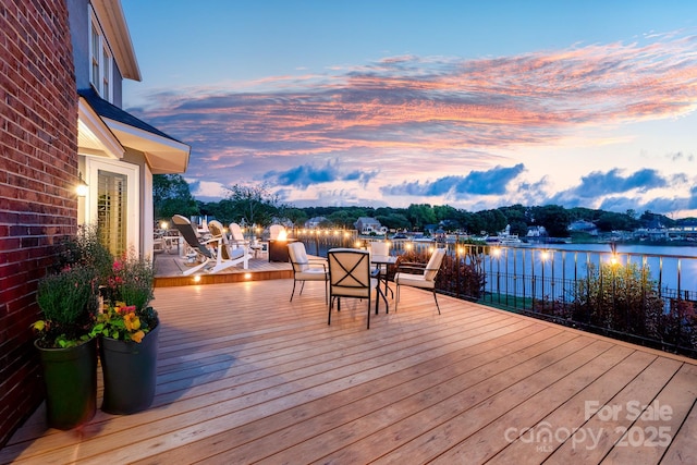 wooden terrace with a water view and outdoor dining space