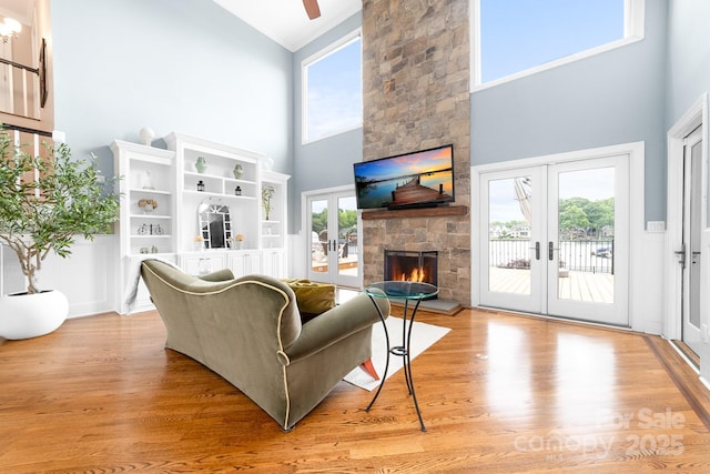 living room featuring light wood-type flooring, french doors, a fireplace, and high vaulted ceiling