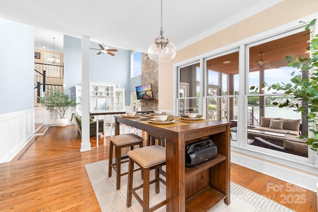 dining room featuring a wainscoted wall, light wood-style floors, ceiling fan with notable chandelier, and ornamental molding