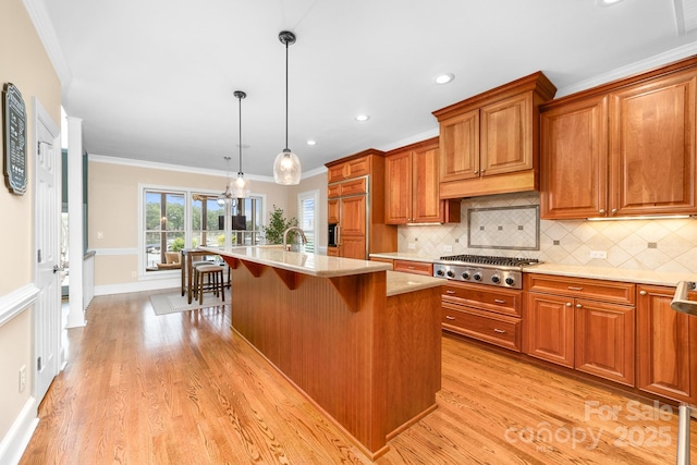 kitchen with brown cabinets, backsplash, light countertops, stainless steel gas stovetop, and ornamental molding