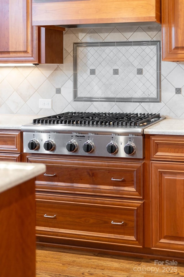 kitchen featuring brown cabinets, tasteful backsplash, stainless steel gas stovetop, and custom range hood