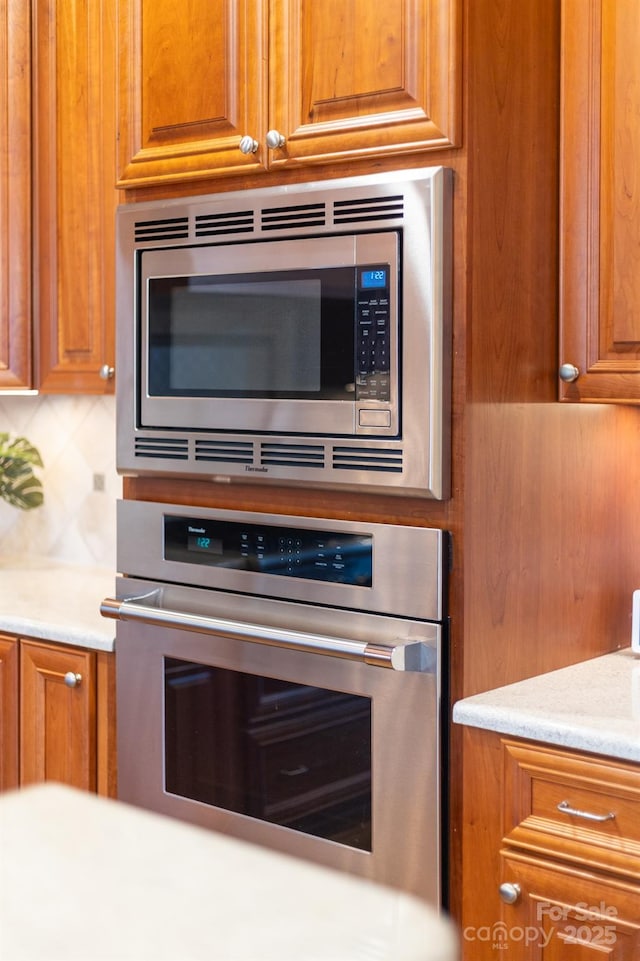 room details featuring appliances with stainless steel finishes, brown cabinetry, and tasteful backsplash
