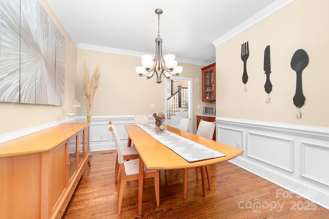 dining room featuring light wood finished floors, a decorative wall, ornamental molding, and a notable chandelier