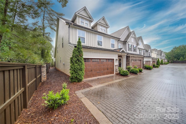view of side of home featuring board and batten siding, fence, a residential view, an attached garage, and decorative driveway