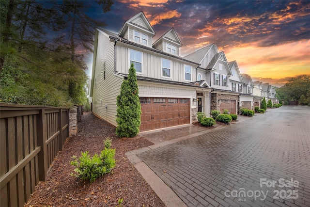 view of side of home featuring board and batten siding, fence, decorative driveway, an attached garage, and a residential view