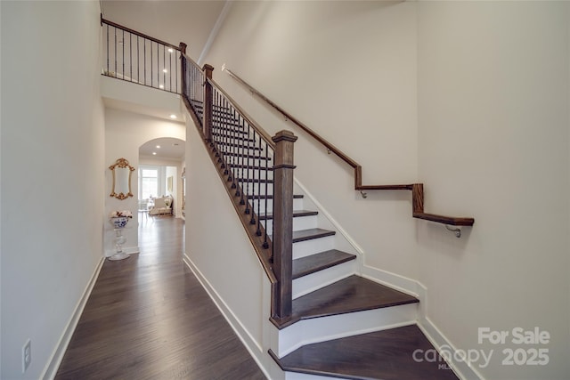 stairway with arched walkways, wood finished floors, baseboards, and a high ceiling
