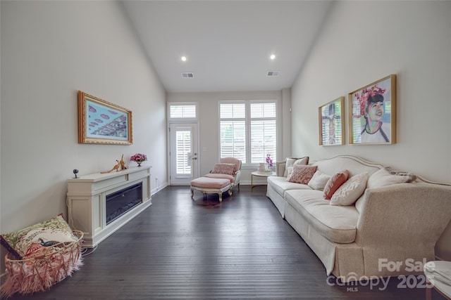 living room featuring dark wood-style floors, recessed lighting, a glass covered fireplace, baseboards, and high vaulted ceiling