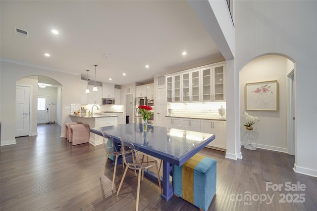 dining space with arched walkways, baseboards, dark wood finished floors, and recessed lighting