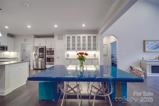 dining space with arched walkways, dark wood-type flooring, and recessed lighting