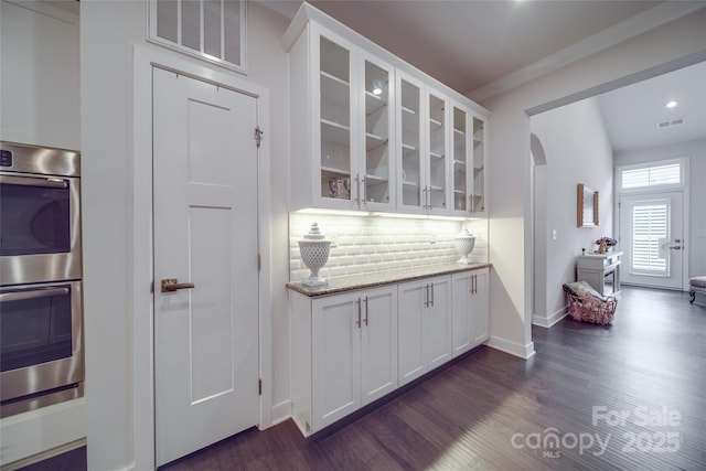 kitchen featuring arched walkways, stainless steel double oven, white cabinetry, backsplash, and recessed lighting