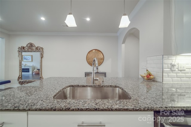 kitchen with a sink, crown molding, stone countertops, arched walkways, and tasteful backsplash