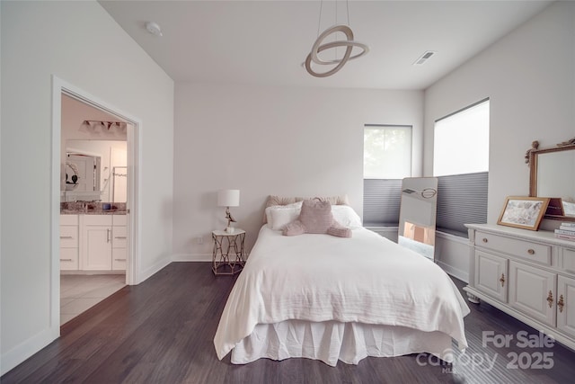 bedroom featuring dark wood finished floors, baseboards, ensuite bath, and a sink